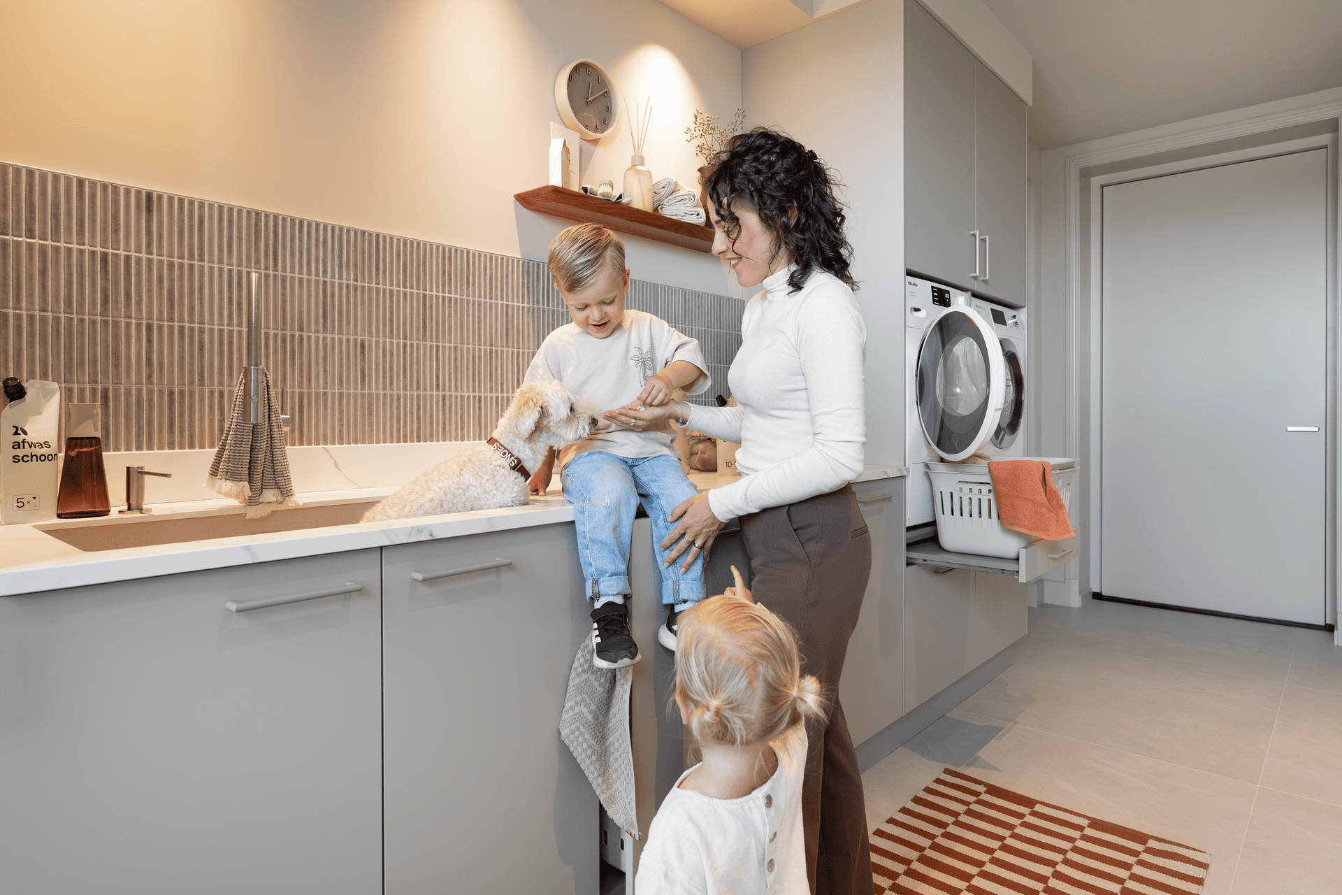 Vrouw met kinderen en hong in de bijkeuken met een wasmachinekast op de achtergrond